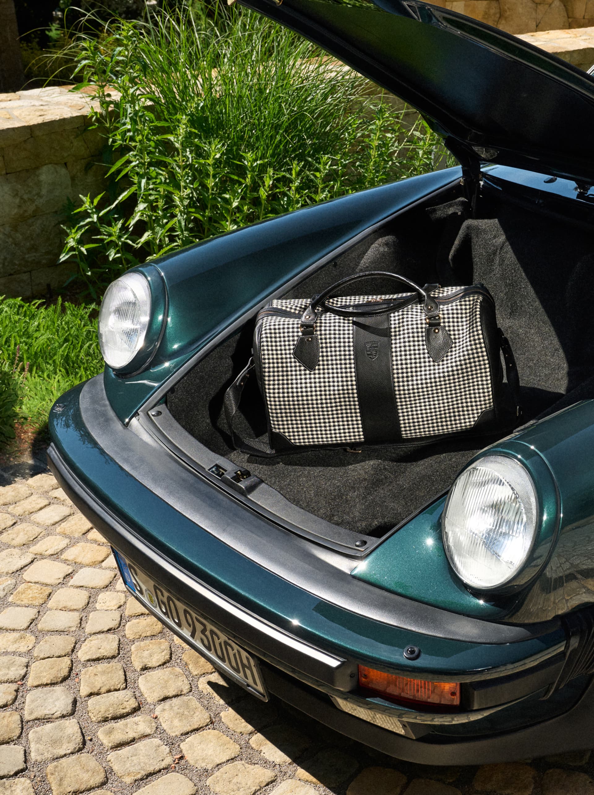 Zwart-wit geruite reistas met zwarte lederen details in de open kofferbak van een groene Porsche.