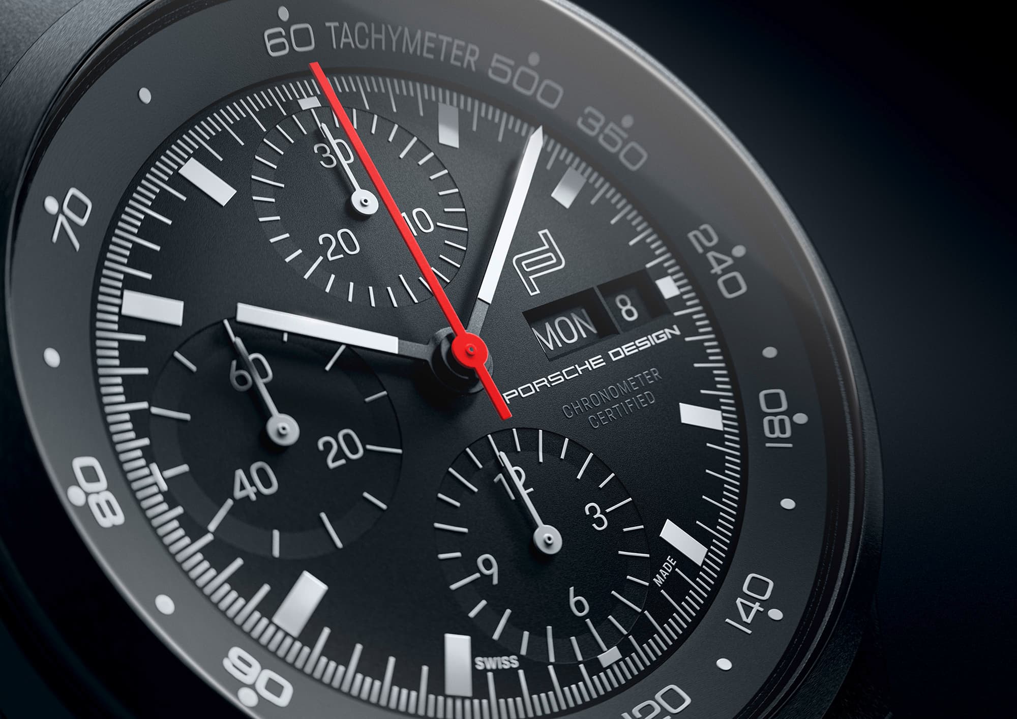 Zbliżenie na czarny chronograf Porsche Design z czerwoną wskazówką sekundową i skalą tachymetru.