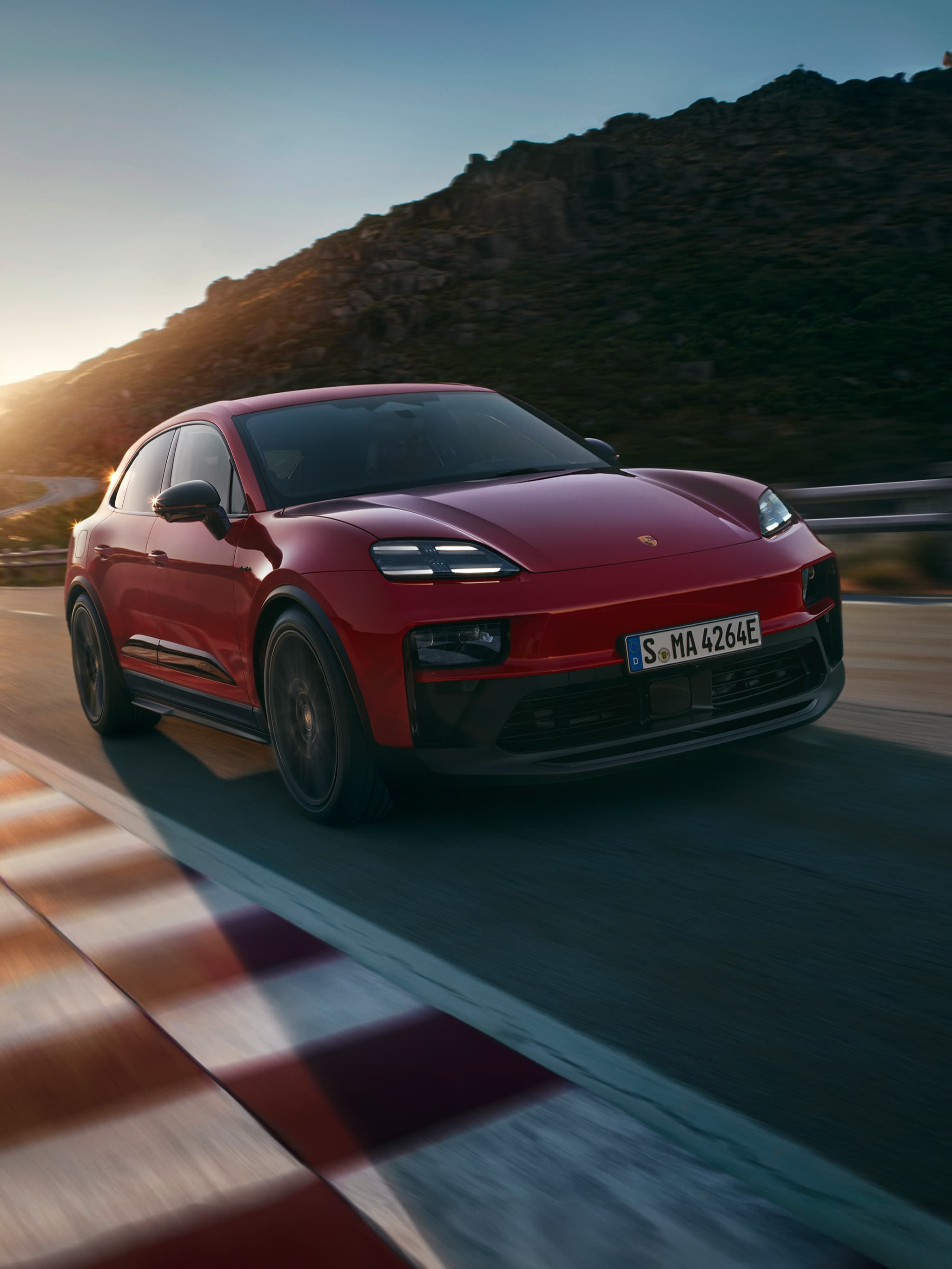 Porsche Macan rosso che percorre una strada di montagna tortuosa al tramonto, vista frontale con effetto mosso.