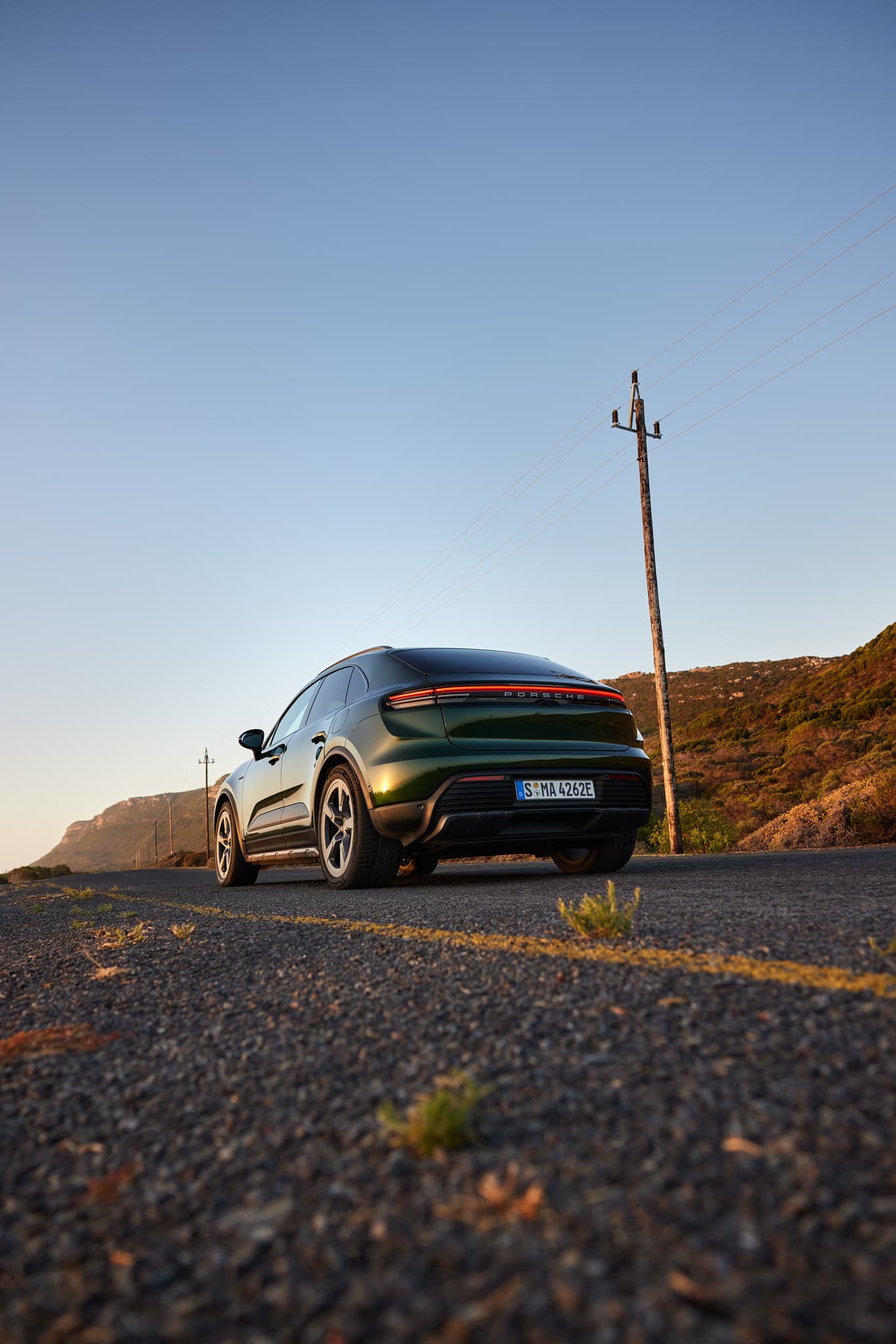 Porsche Macan rouge roulant au coucher du soleil sur une route de montagne sinueuse, vue de face avec flou de mouvement.