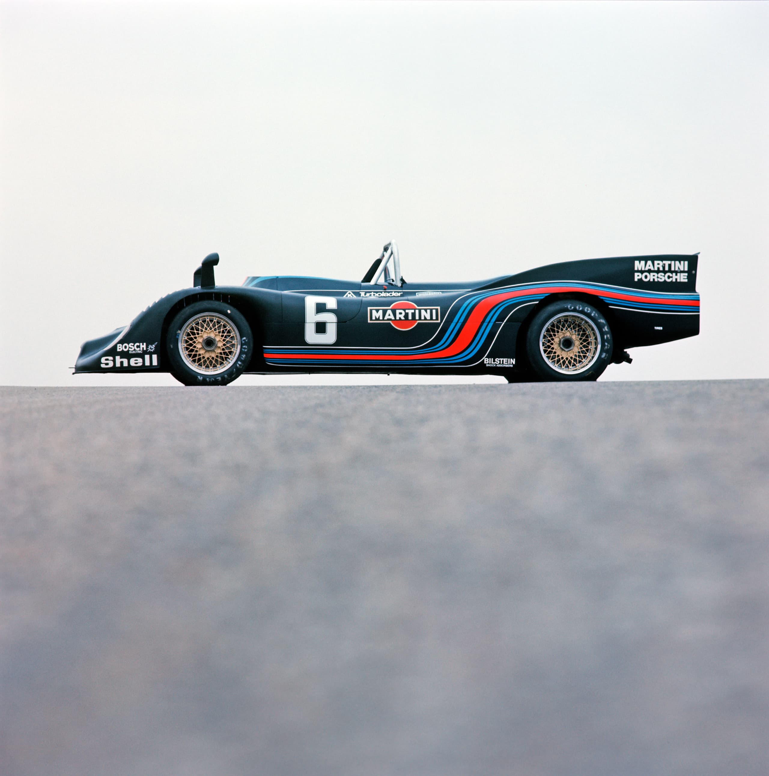 Vintage Porsche race car with Martini livery, number 6, side view on a flat surface, clear sky background.