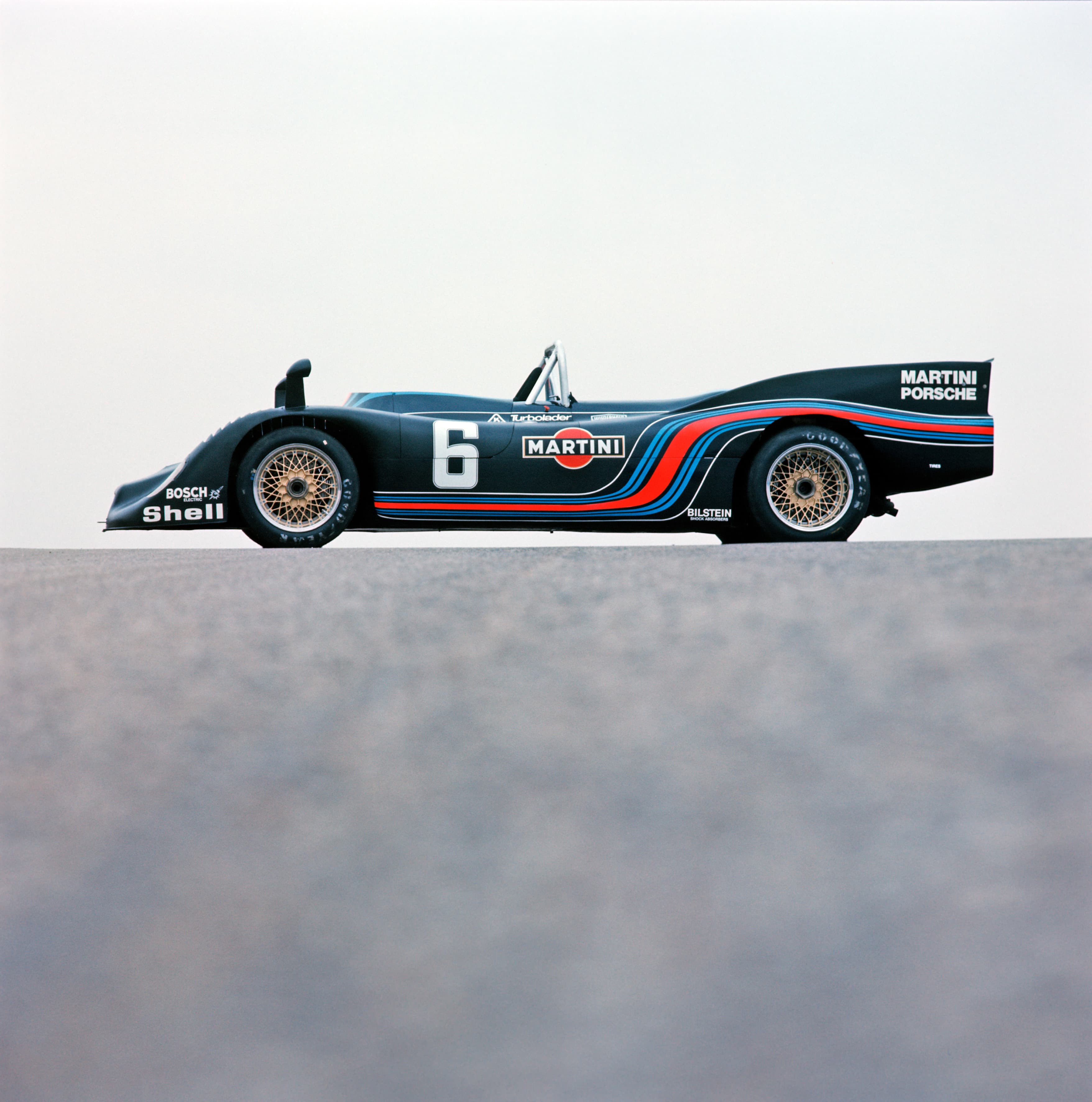 Vintage Porsche Rennwagen mit Martini-Lackierung, Nummer 6, Seitenansicht auf ebener Fläche, klarer Himmel im Hintergrund.