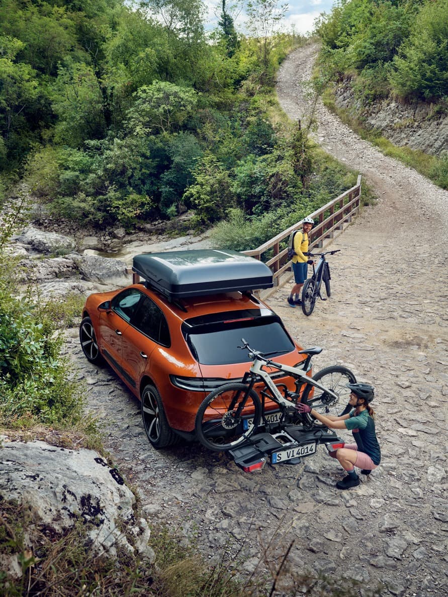 You can see an orange Porsche car with a roof box and a bike rack in the nature