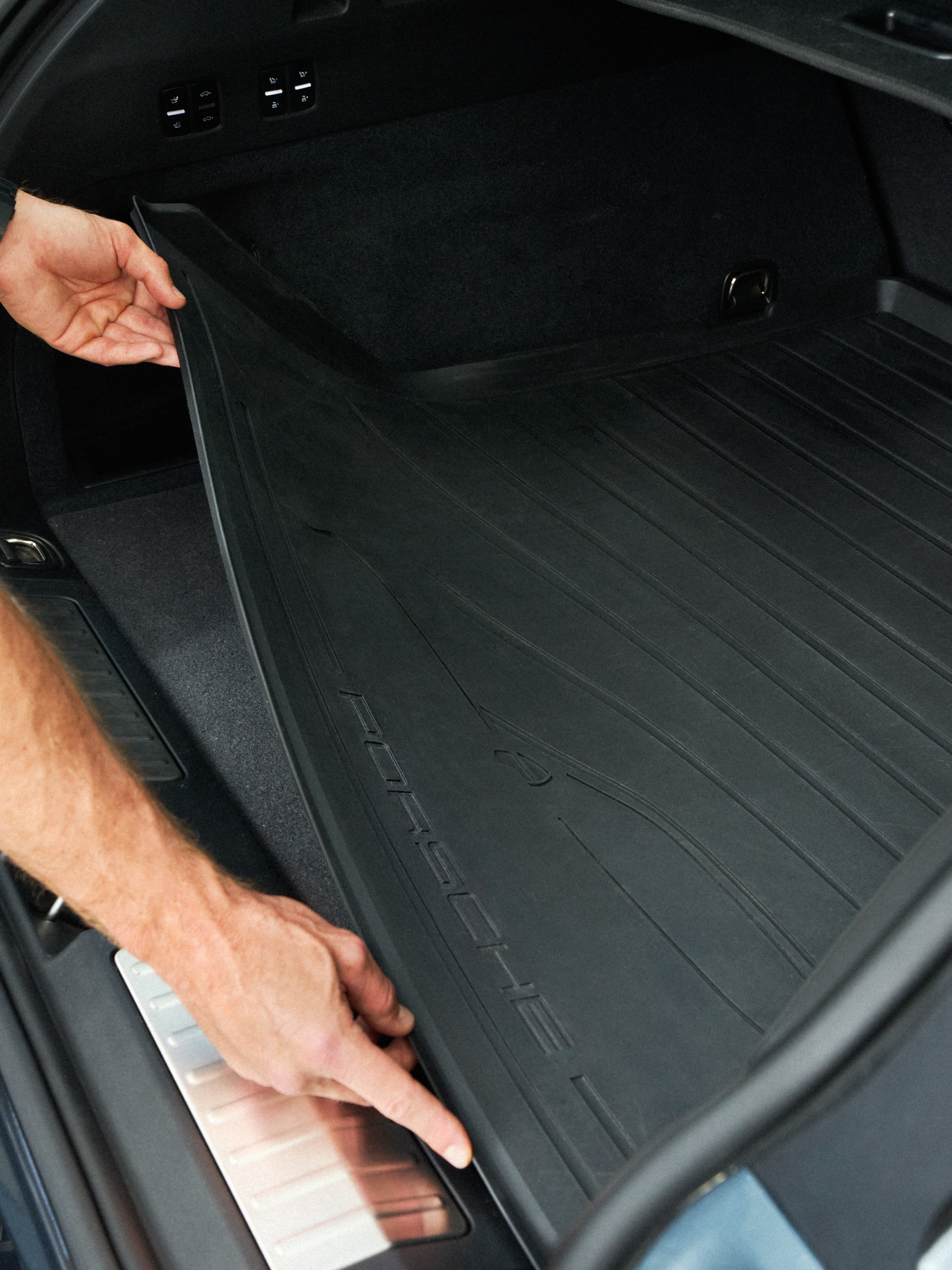 Mano che posiziona un rivestimento nero in gomma per il bagagliaio nell’area di carico di una Porsche, primo piano della superficie testurizzata del tappetino e della soglia posteriore.