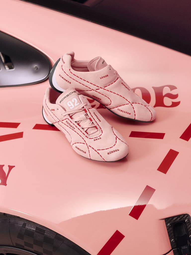 Pink sneakers with red stitching and text, placed on a matching pink car hood with red accents.