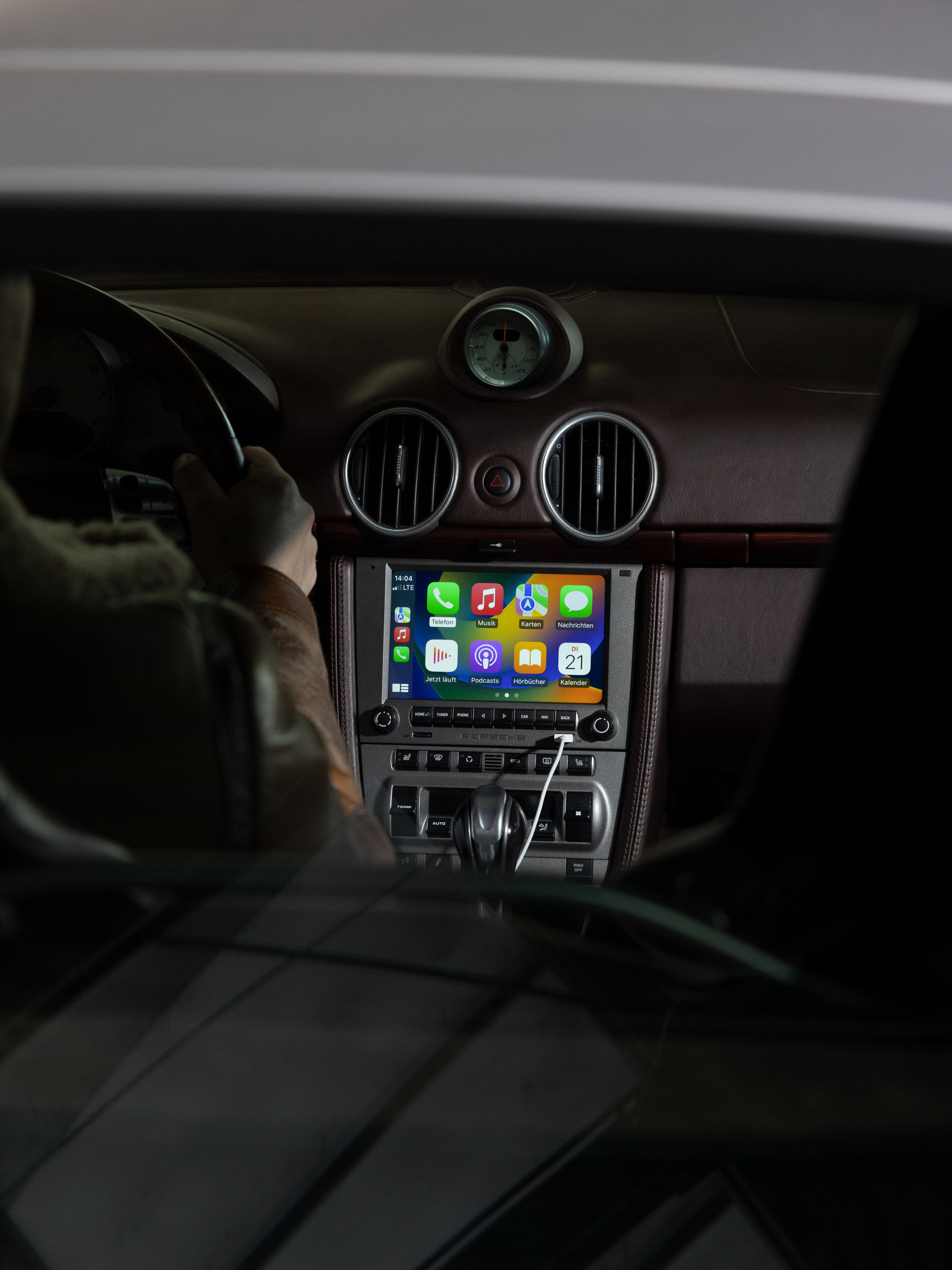 Car interior with a digital display showing app icons, steering wheel, and dashboard with circular vents and clock.