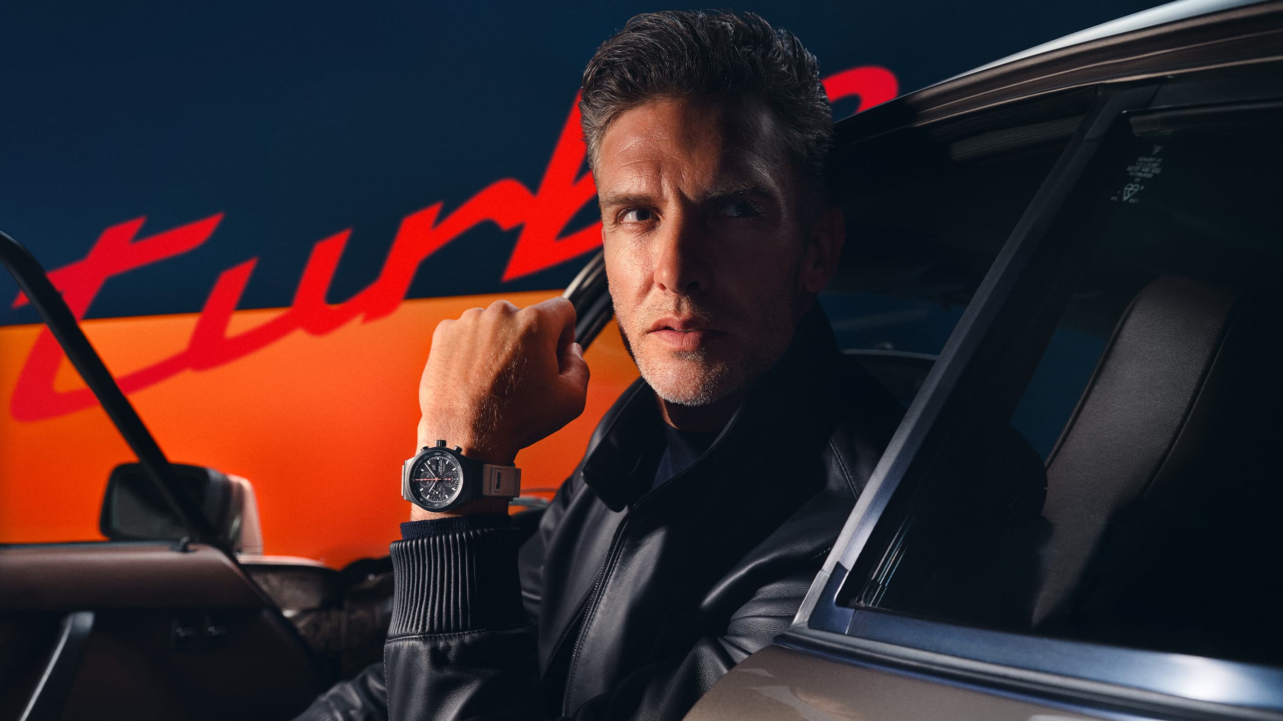 Man is sitting in a car and wearing 50Y chronograph with turbo lettering in the background