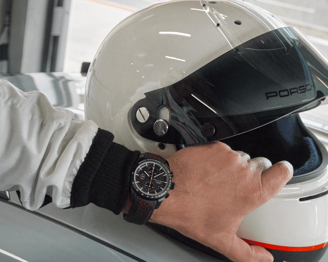 Mężczyzna w zegarku na rękę Porsche Chronograph 1 GT3 RS, trzymający biały kask.