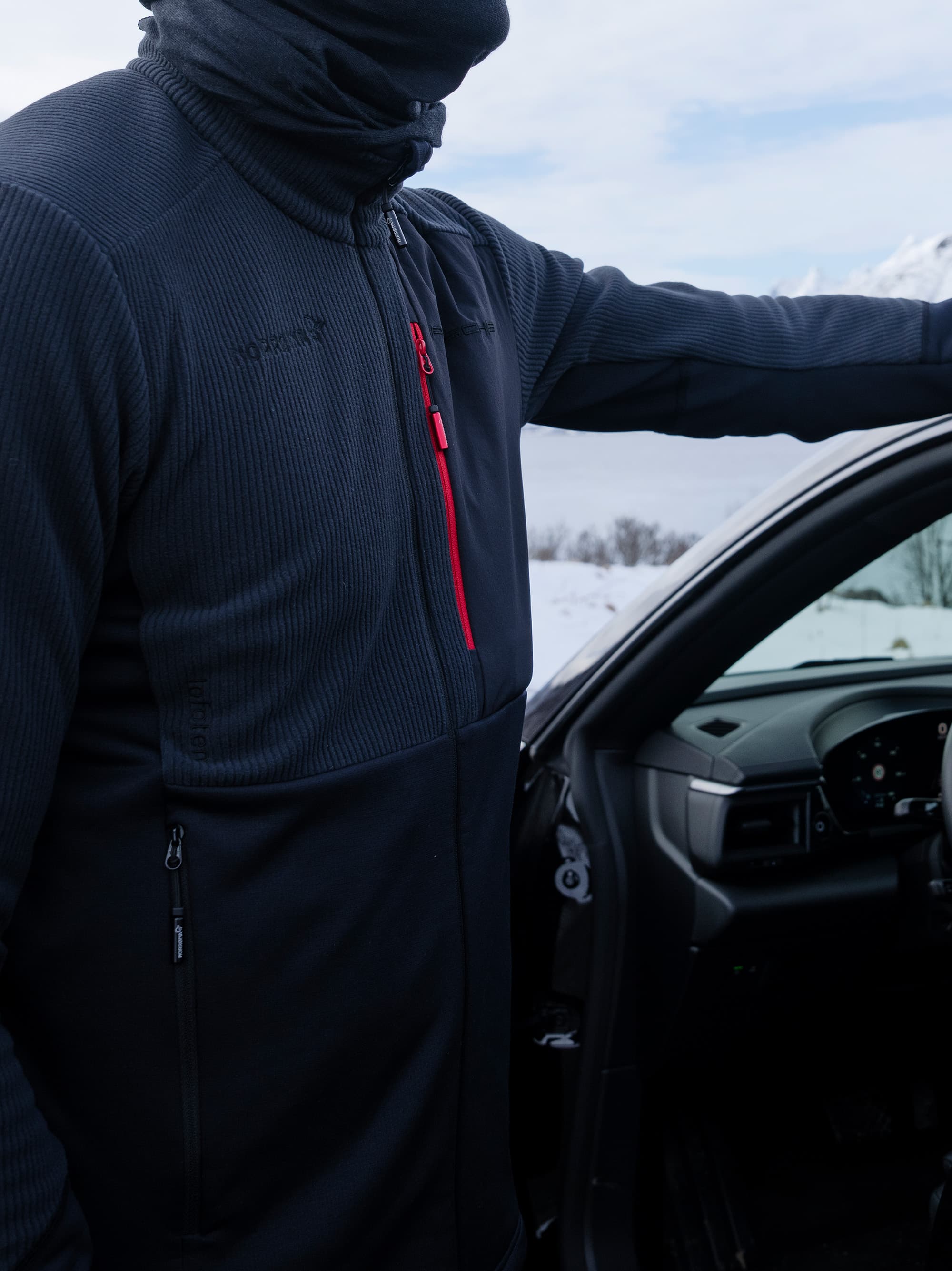 Man wearing Porsche x Norrøna Skiwear, Porsche car in background