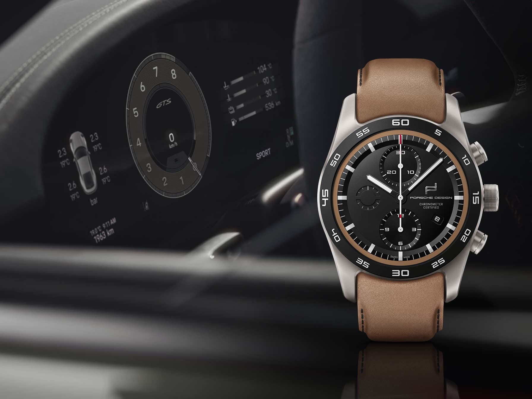 Zegarek chronograf Porsche Design z czarną tarczą i brązowym skórzanym paskiem, na tle rozmytej deski rozdzielczej Porsche.