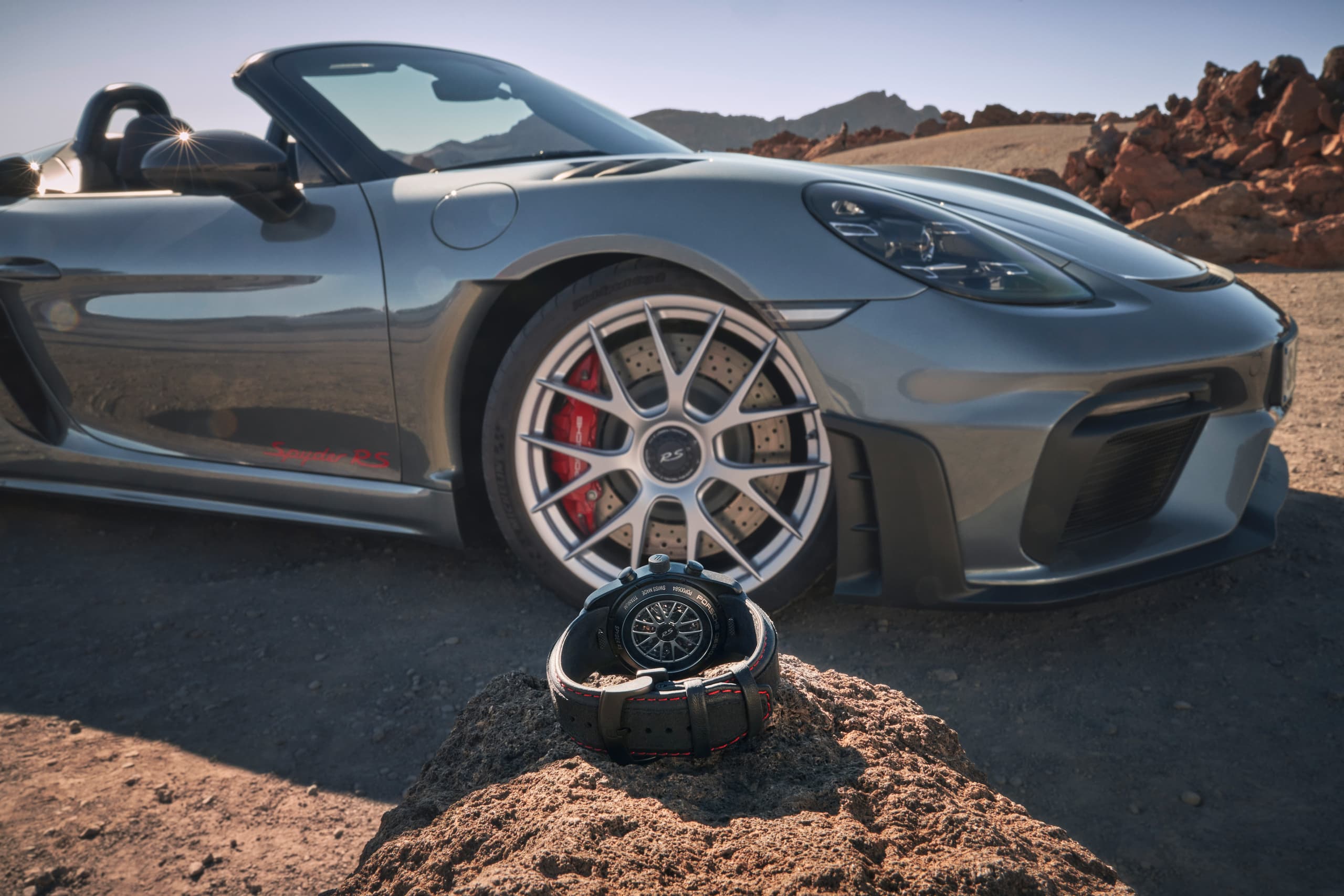 Chronograf Porsche 718 Spyder RS widziany od tyłu na kamieniu; w tle niebieski Porsche 718 Spyder