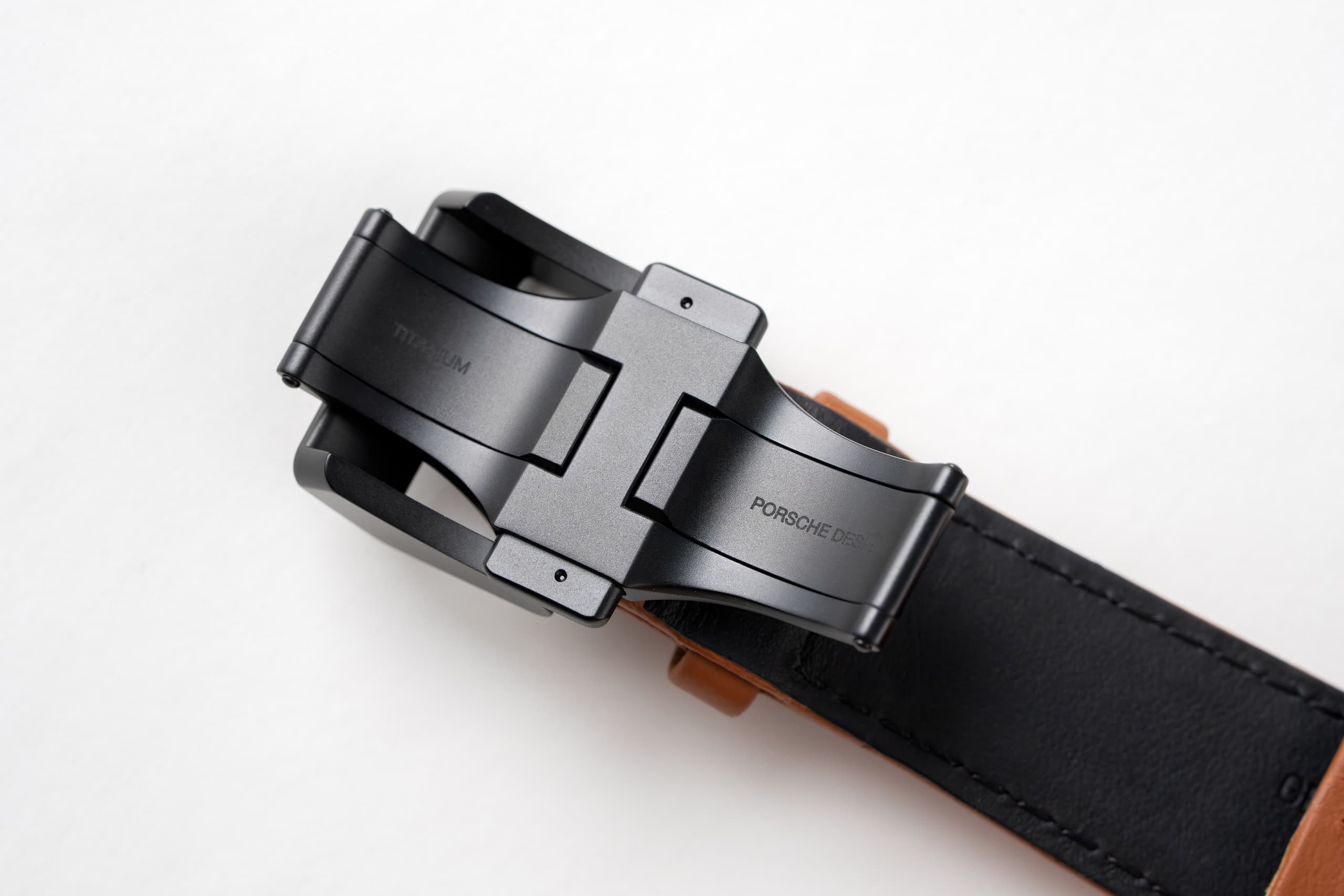 Ceinture en cuir noir avec boucle en métal noir mat et gravure Porsche Design, gros plan sur fond blanc.