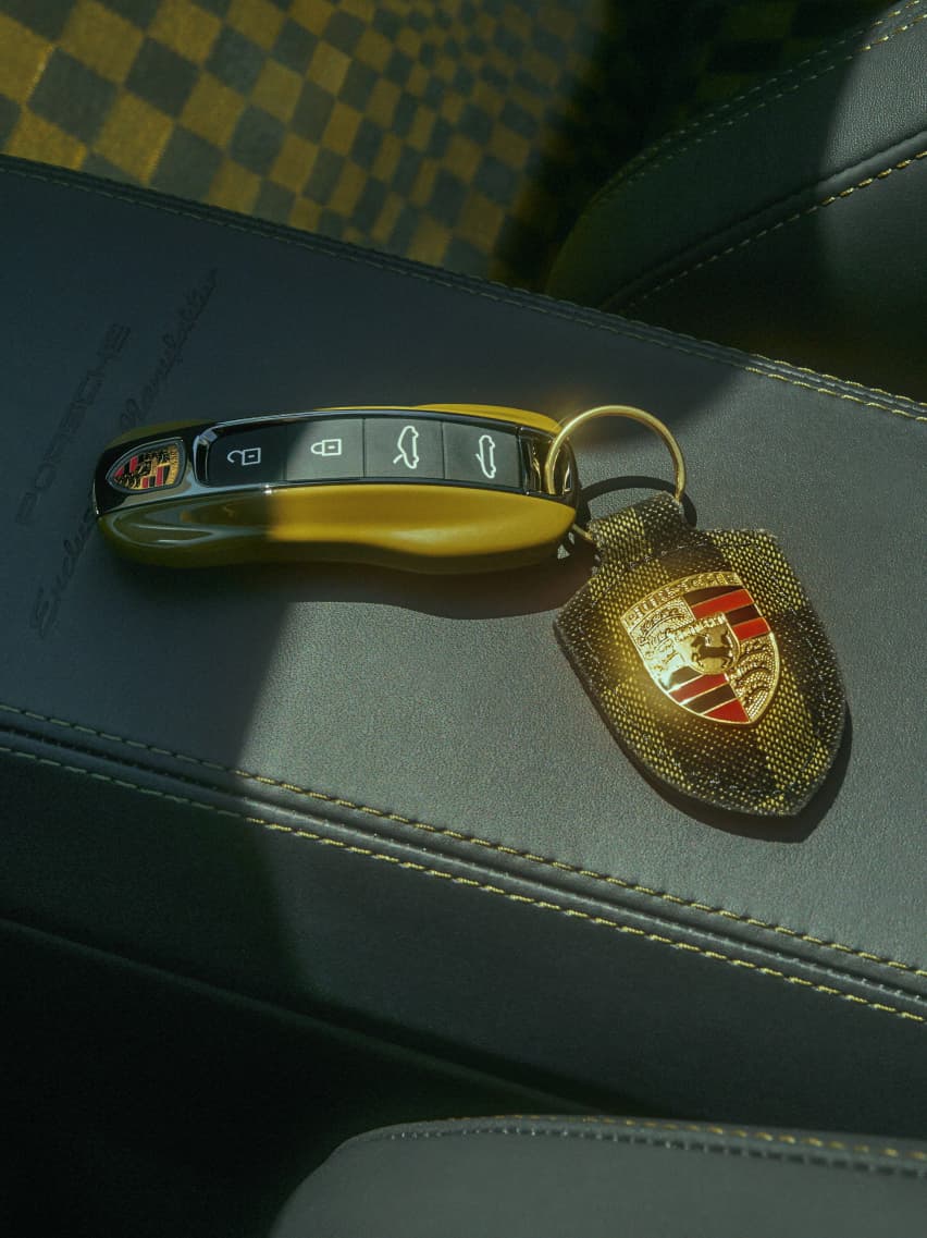 Porsche key with Porsche crest pendant with Pasha pattern in Olive Neo is located on the middle console in the car