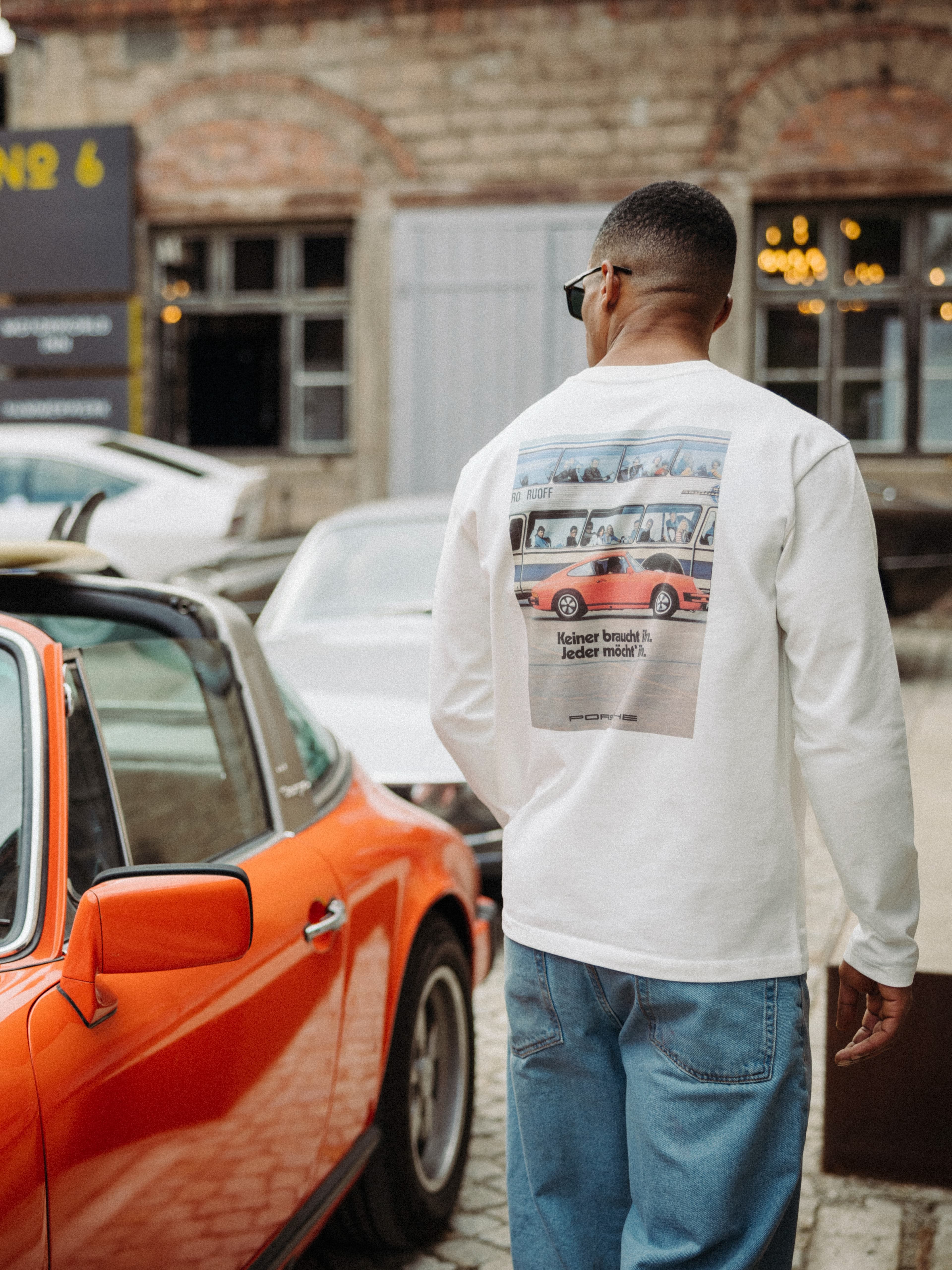 A man standing next to a orange Porsche looking in the distance