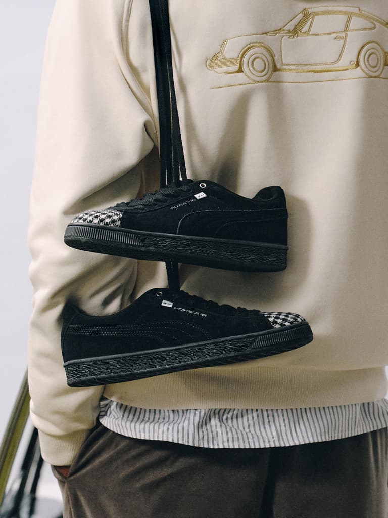 Sneakers Porsche nere con puntale a motivo pied-de-poule, con lacci neri, davanti a una felpa con cappuccio beige con stampa auto.