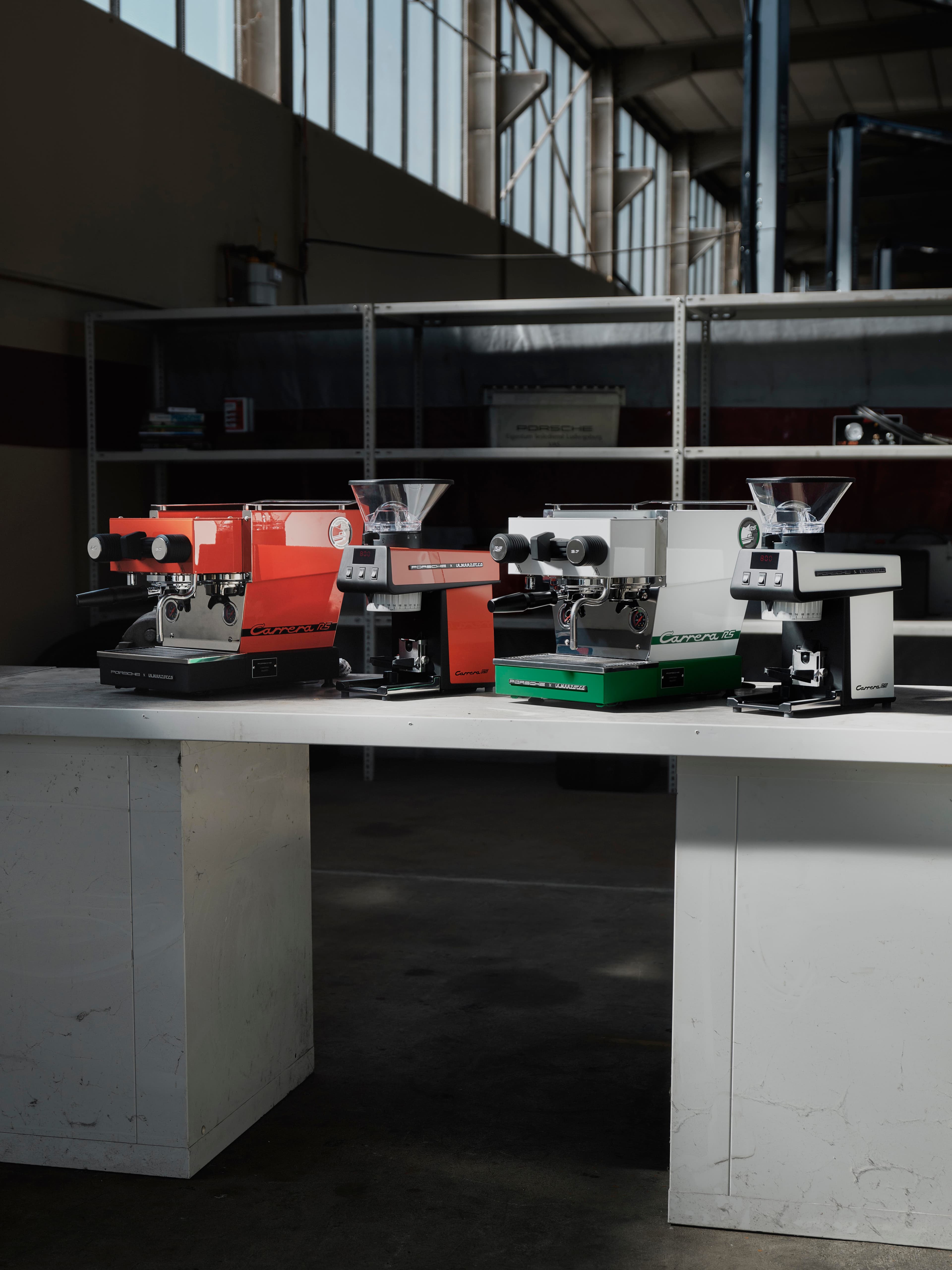 Vier Porsche x La Marzocco Maschinen in Orange, Grün und Weiß auf einer Werkbank in einer Industriehalle.