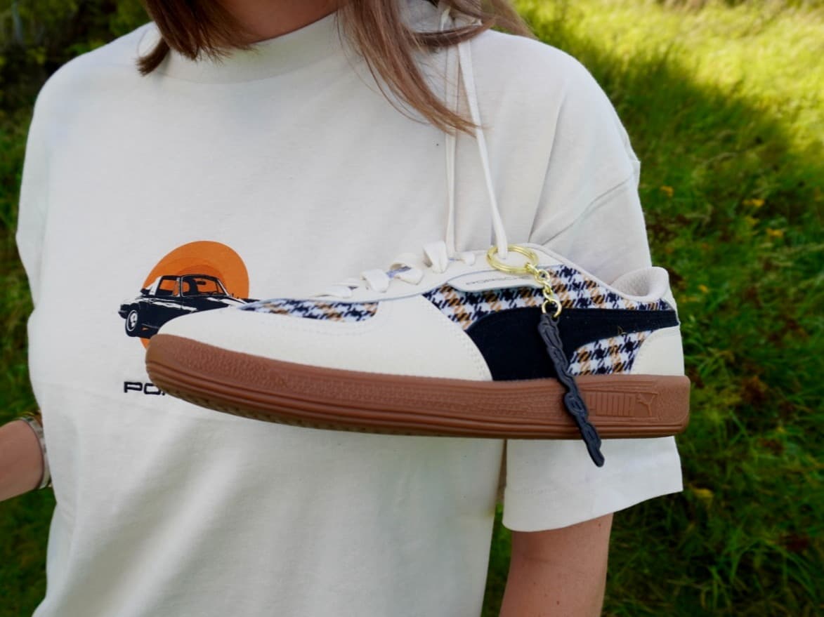 White sneaker with plaid pattern and brown sole, hanging from a white shirt with a Porsche car graphic, outdoors.