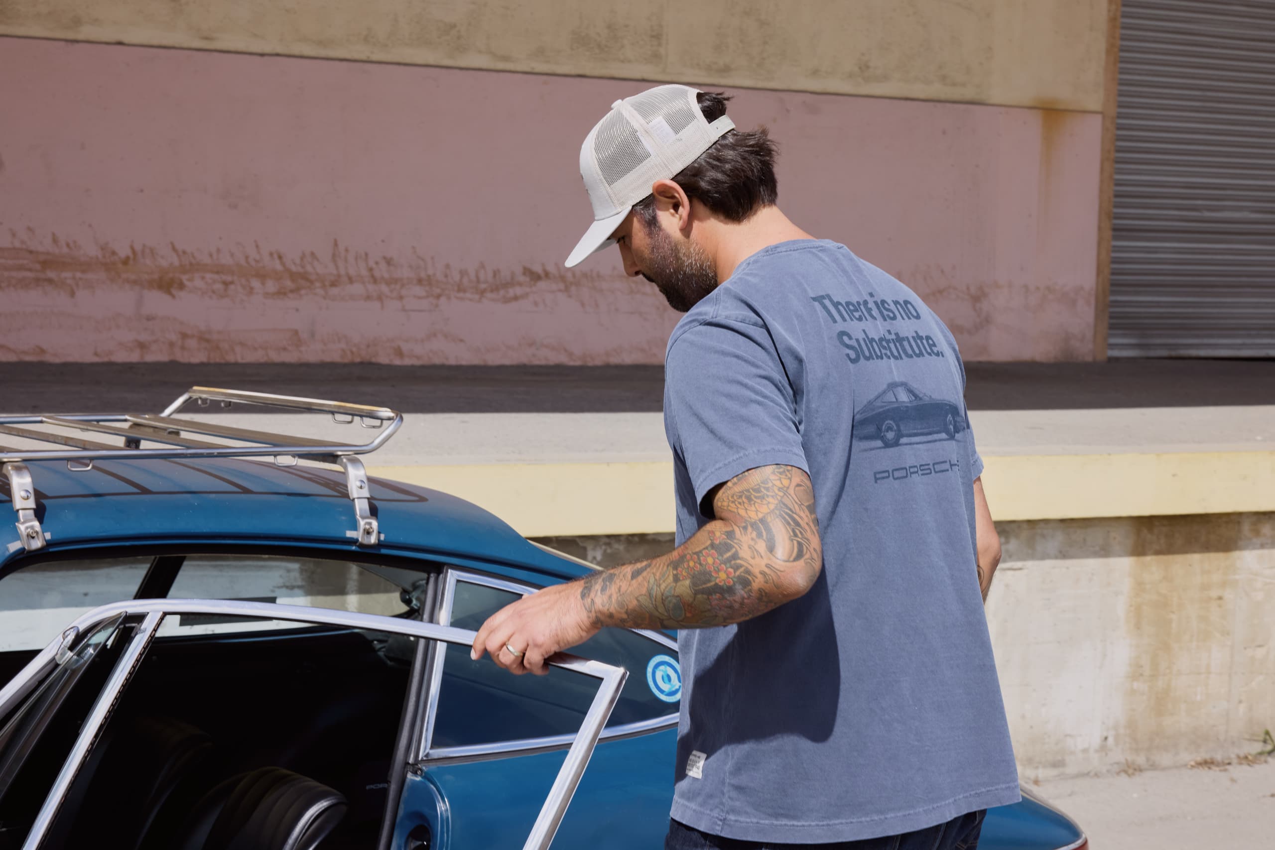 Male Model Wearing a blue TINS T-Shirt entering a blue Porsche.