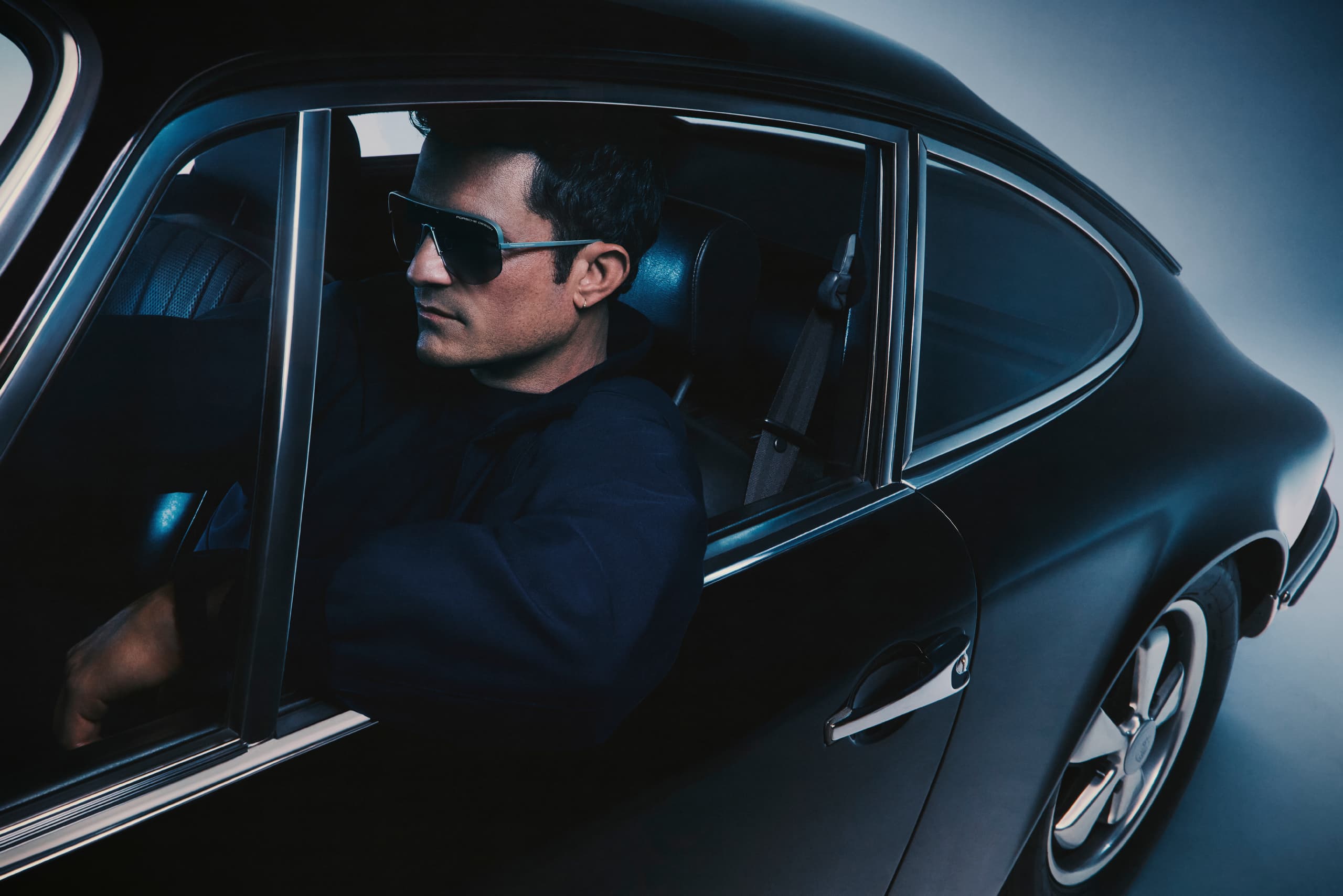 Orlando Bloom sitting in a black Porsche 911 Targa, wearing the Porsche Design Iconic Targa Sunnglasses