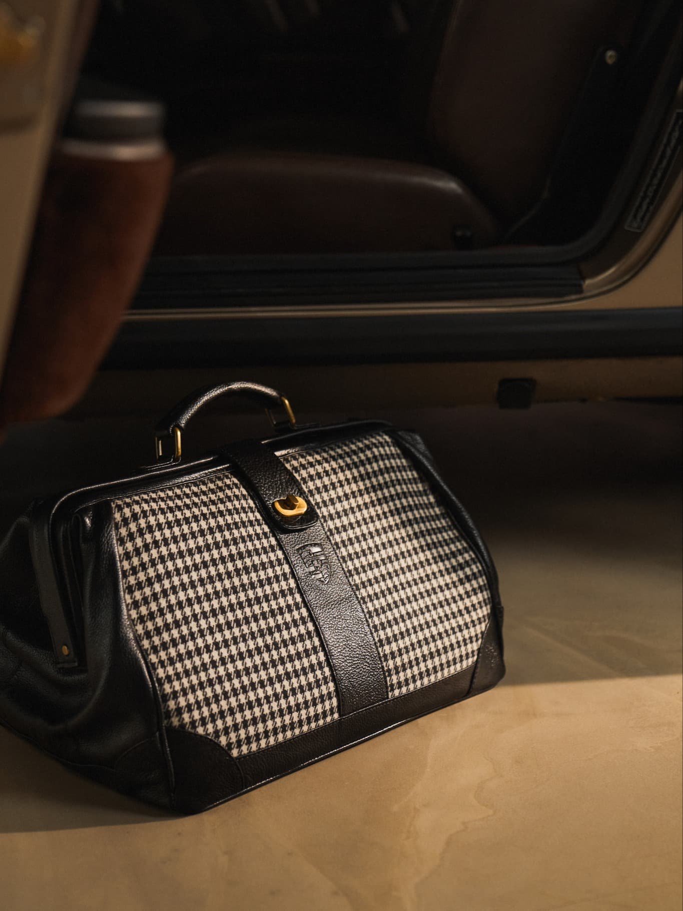 Black-and-white houndstooth bag with black leather details and gold hardware, placed in a car.