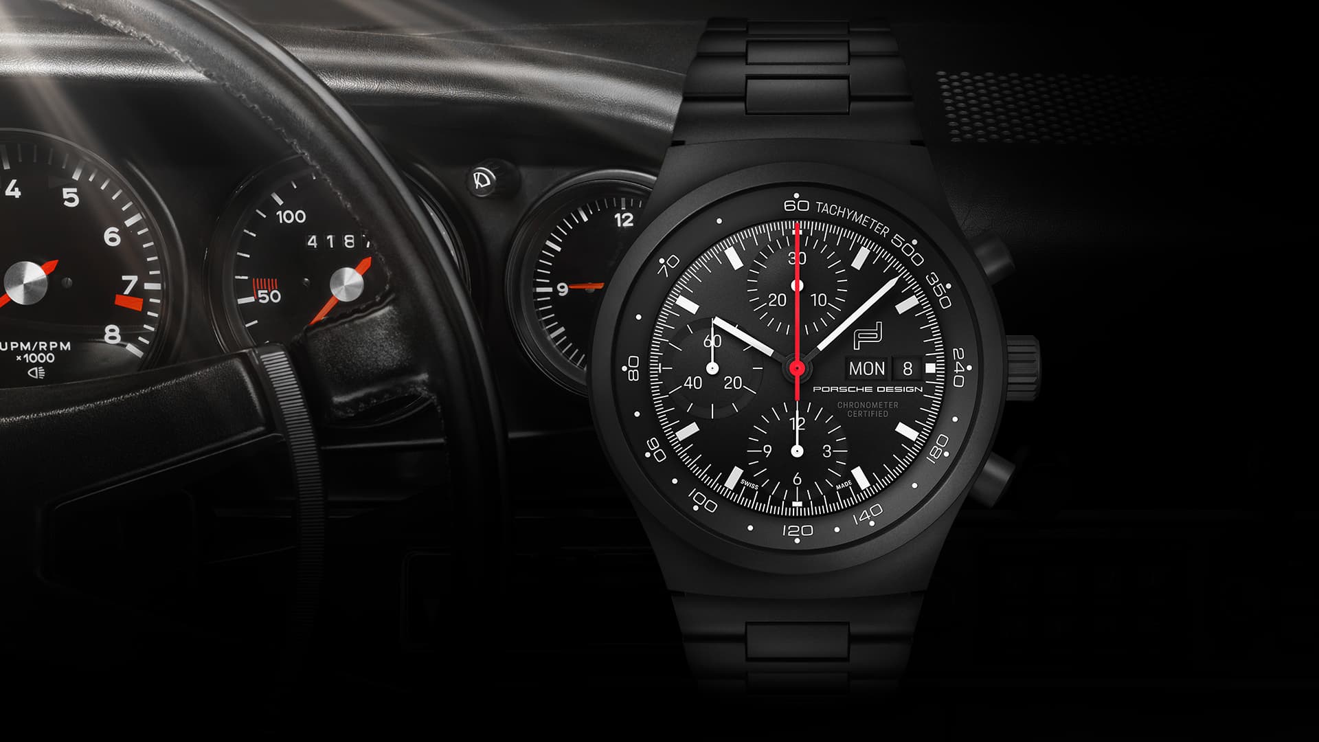 Czarny zegarek chronograf Porsche Design z czerwoną wskazówką sekundową, na tle kokpitu Porsche z wyświetlaczami wskaźników.