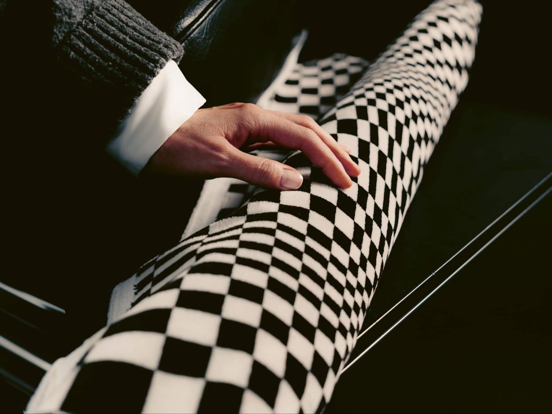 Hand resting on black-and-white checkered fabric inside a car, close-up with dark interior background