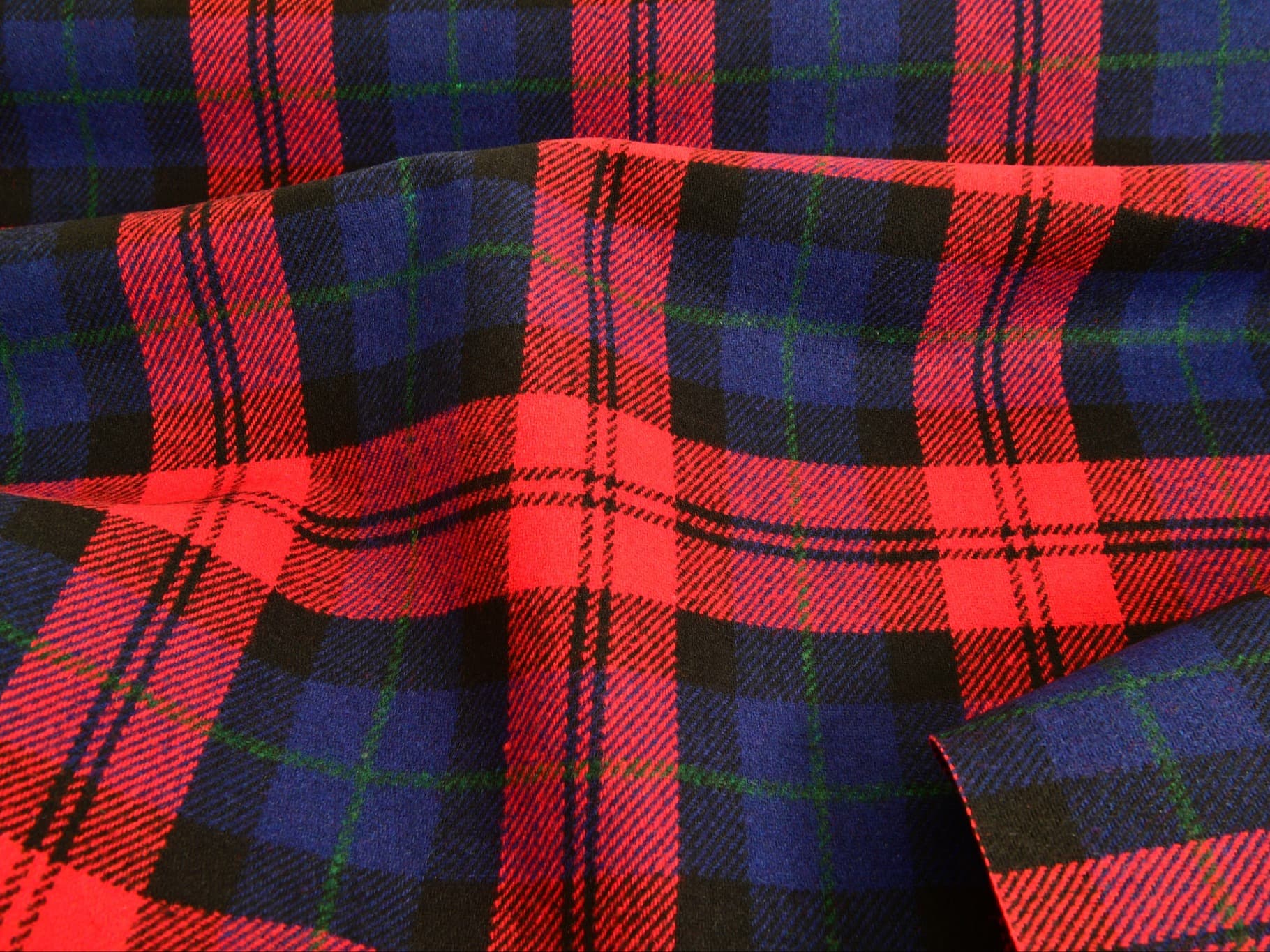 Close-up of red, blue and black tartan fabric with green lines, softly folded to show texture.