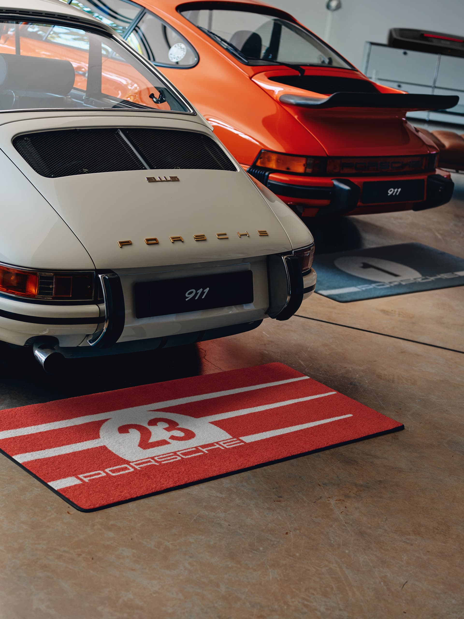 The picture shows a man and a woman in a room. The woman walks by and the man examines the pictures standing on the wall. A white Carrera typewriter is on the wall and a brown leather couch is in the foreground.