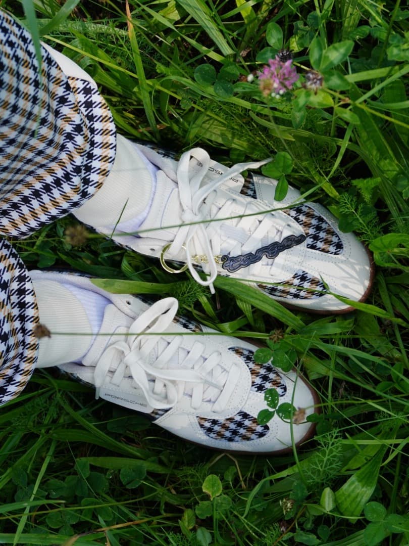 Person holding gray, black, and blue sneakers with colorful stripes, standing on a tiled surface.
