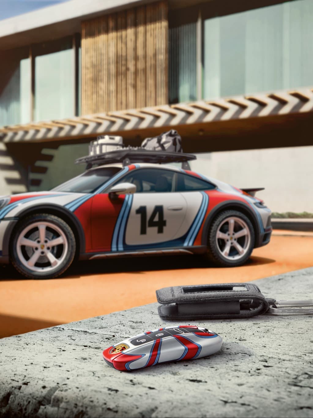Porsche car key in red, white and blue livery on stone surface, with matching race car in background