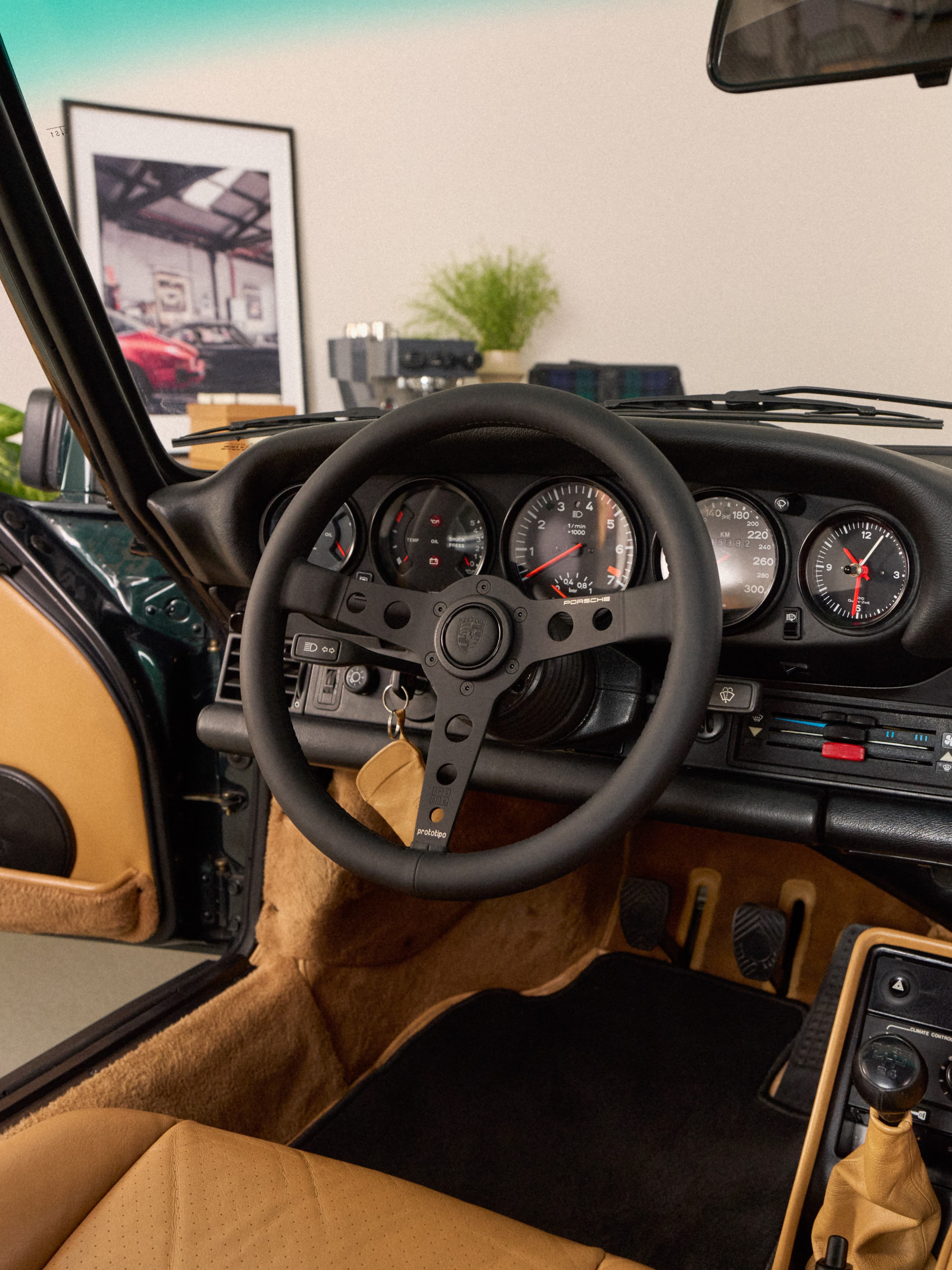 Wnętrze klasycznego Porsche z czarną kierownicą, okrągłymi wskaźnikami i beżową skórzaną tapicerką.