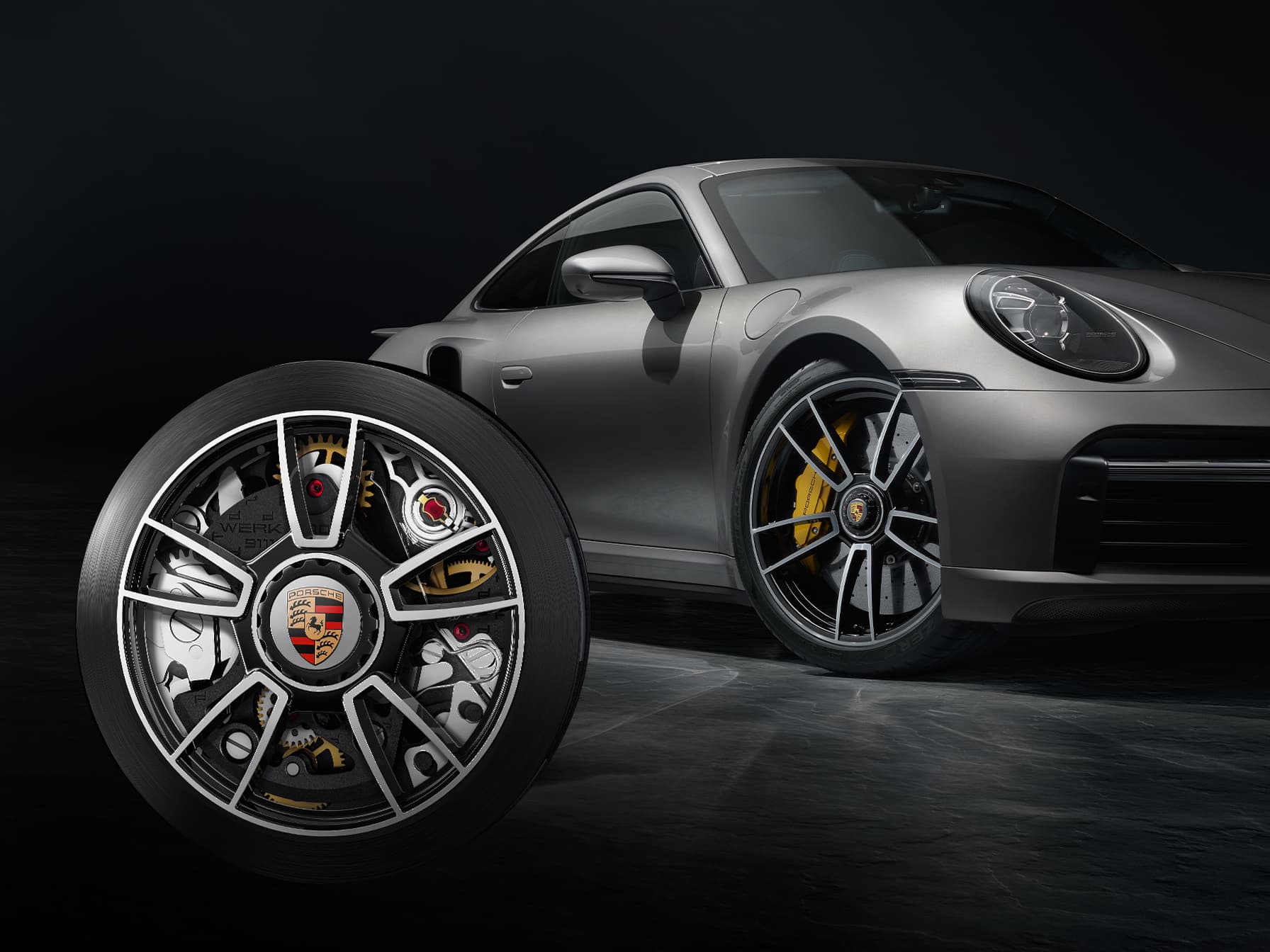 Silberner Porsche 911, Nahaufnahme der Felge im Vordergrund, schwarzer Hintergrund.