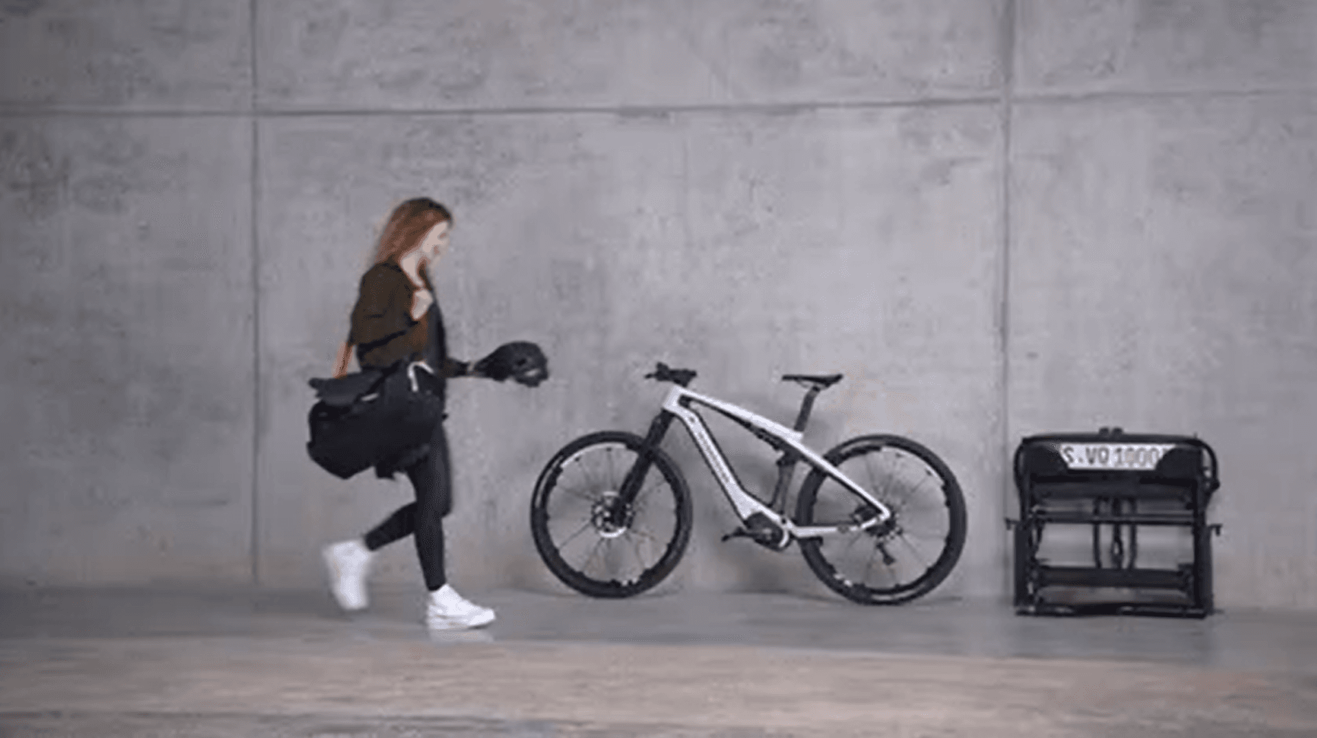 Woman in a garage on the way to her Porsche eBike with a bike rack next to it