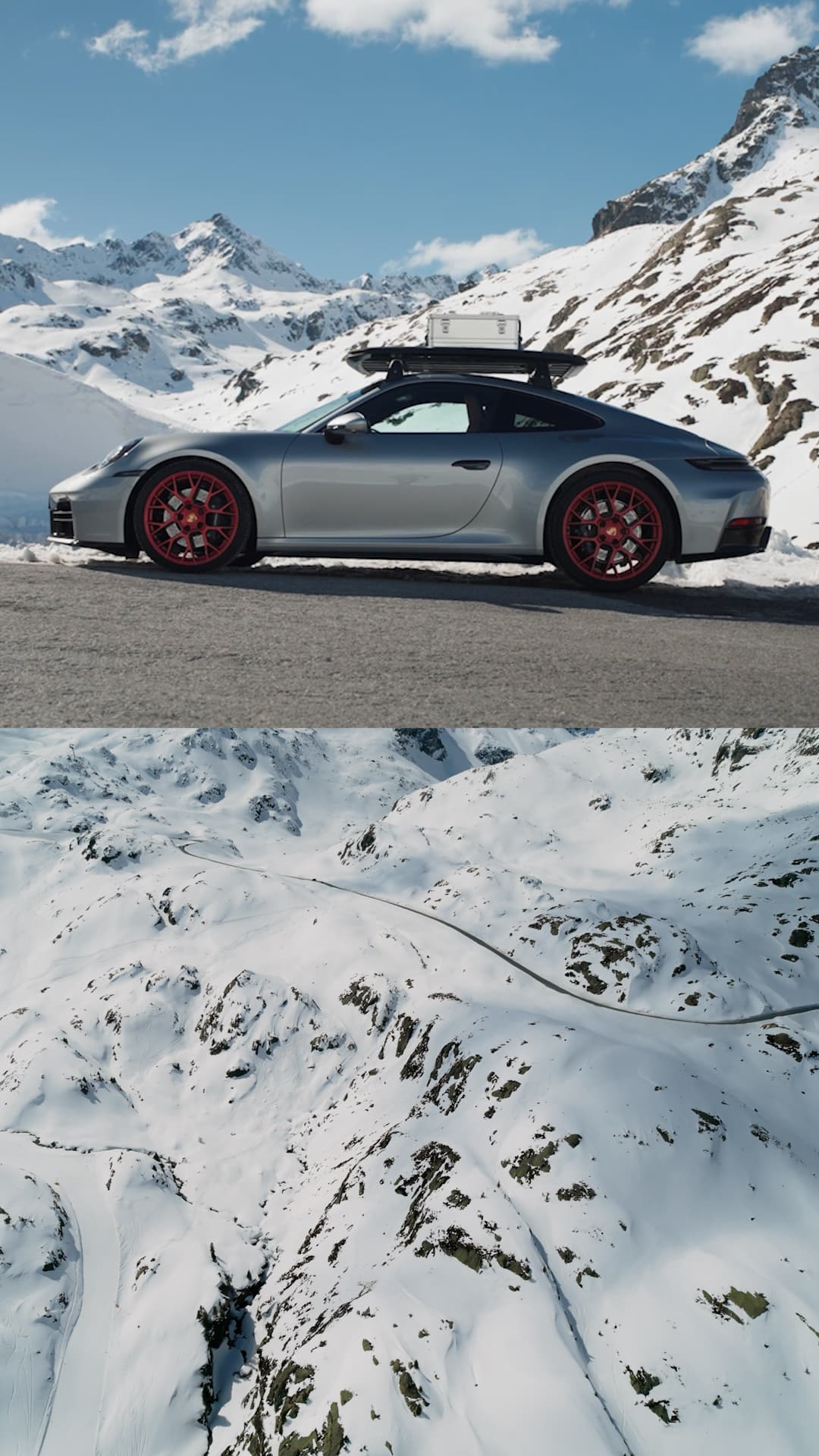 Silver Porsche with red rims on snowy mountain road, roof box attached, under clear blue sky. Snowy peaks in background