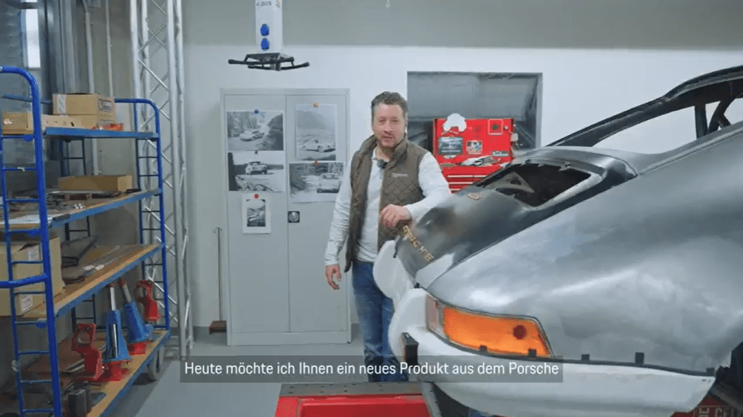 man in a garage next to a historic Porsche car