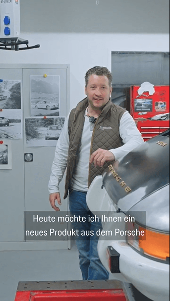 man in a garage next to a historic Porsche car