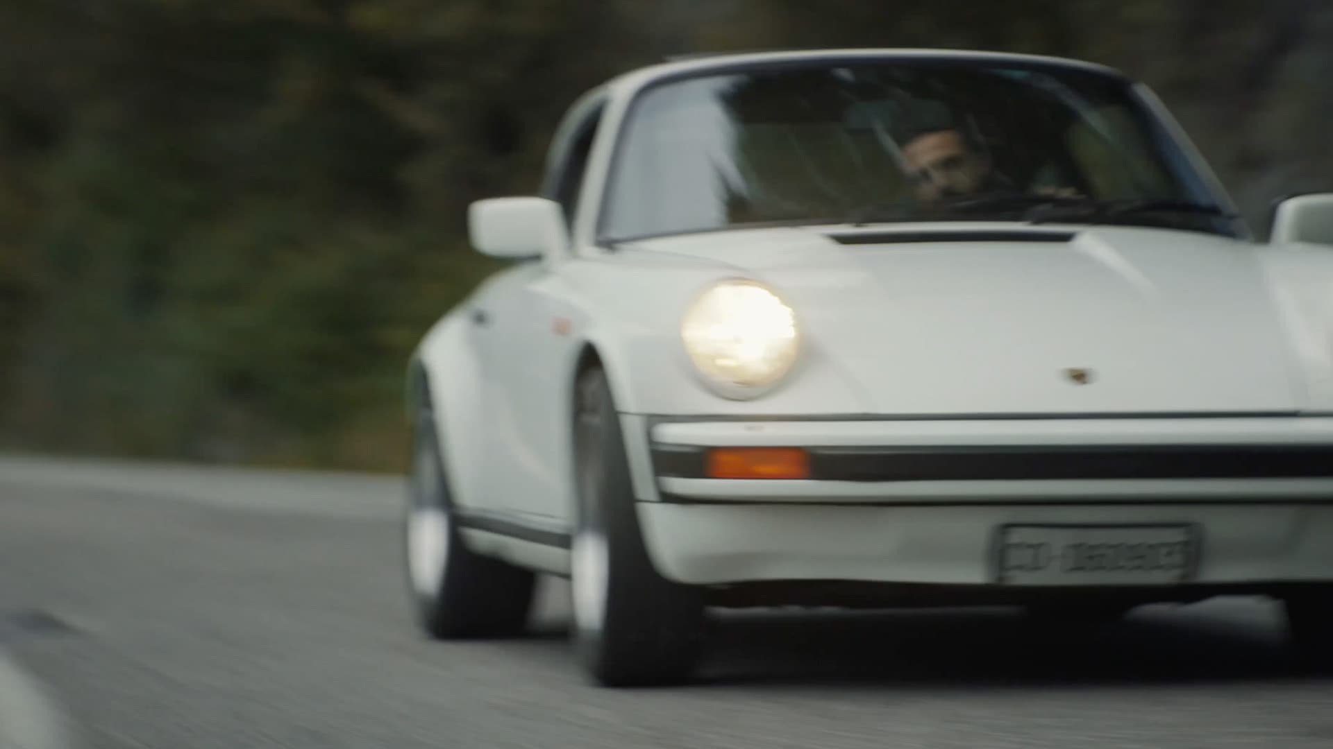 You can see a white historic Porsche 911 driving on the road