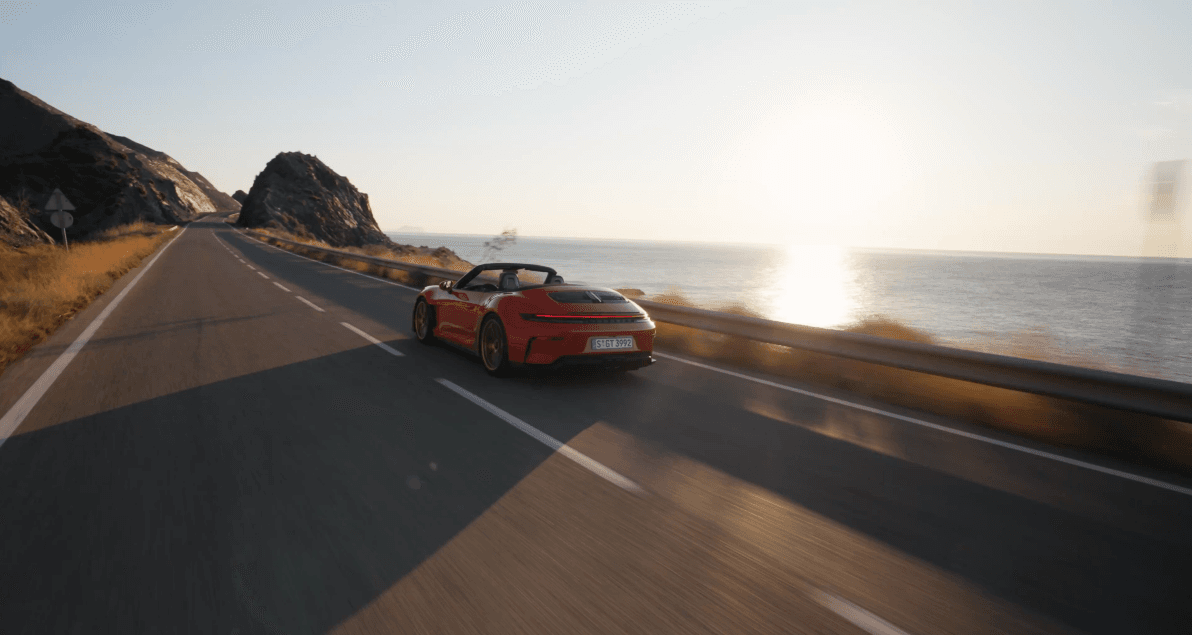 A red Porsche GT3 S/C driving on a road next to the ocean