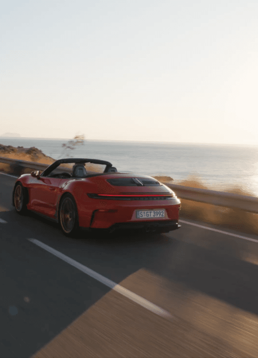 A red Porsche GT3 S/C driving on a road next to the ocean