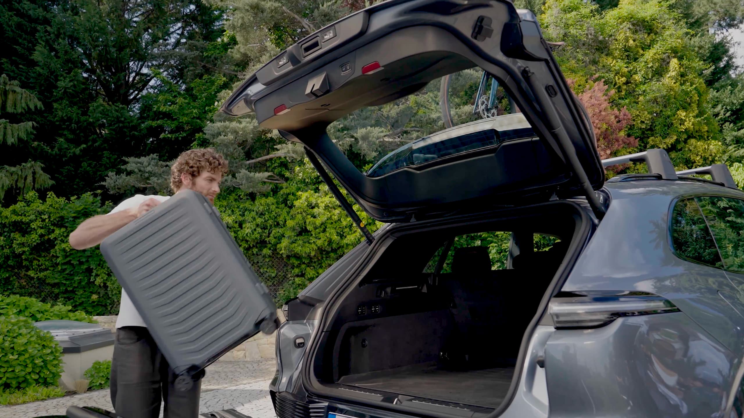 A man is carrying a black Porsche Design suitcase into the boot